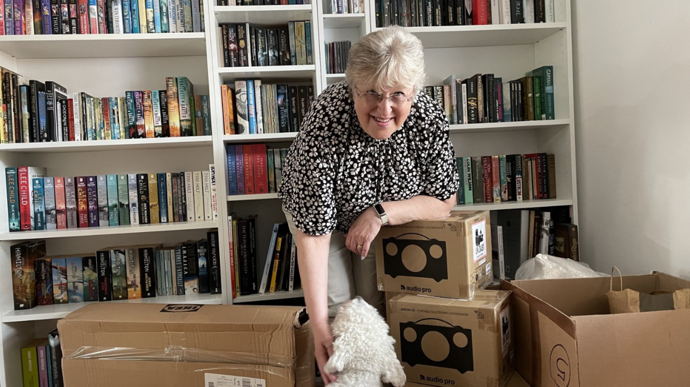 Gail Ward with her dog, surrounded by cardboard boxes in front of a bookcase