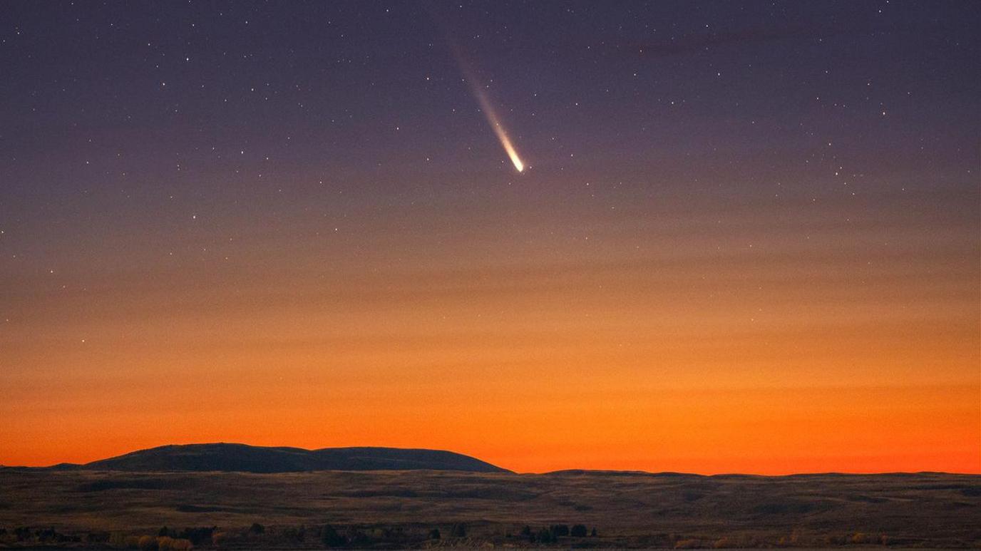 A long-exposure photo of a comet streaking across a night sky.