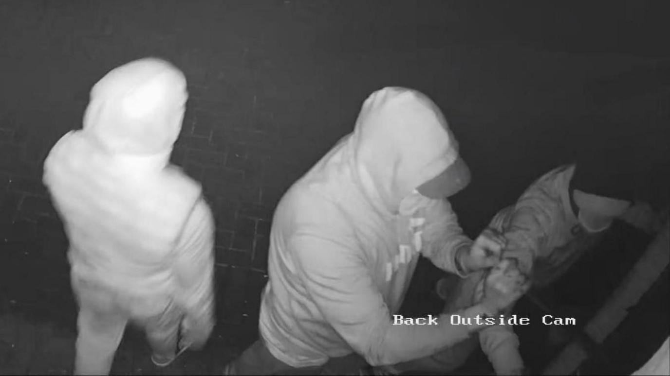 A black and white CCTV still of three hooded people breaking in to the back door at Mother's Kitchen