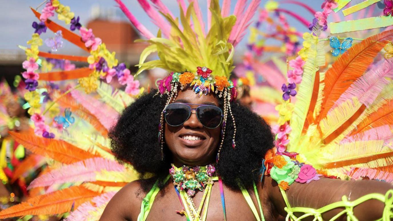 A woman in sunglasses wear a big feathered head piece