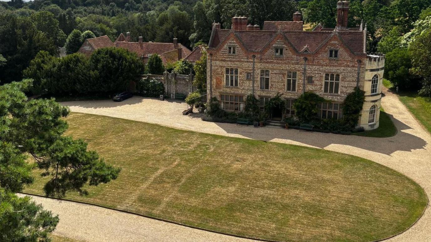 Outlines can be seen on an oval shaped lawn in front of a large stately home.