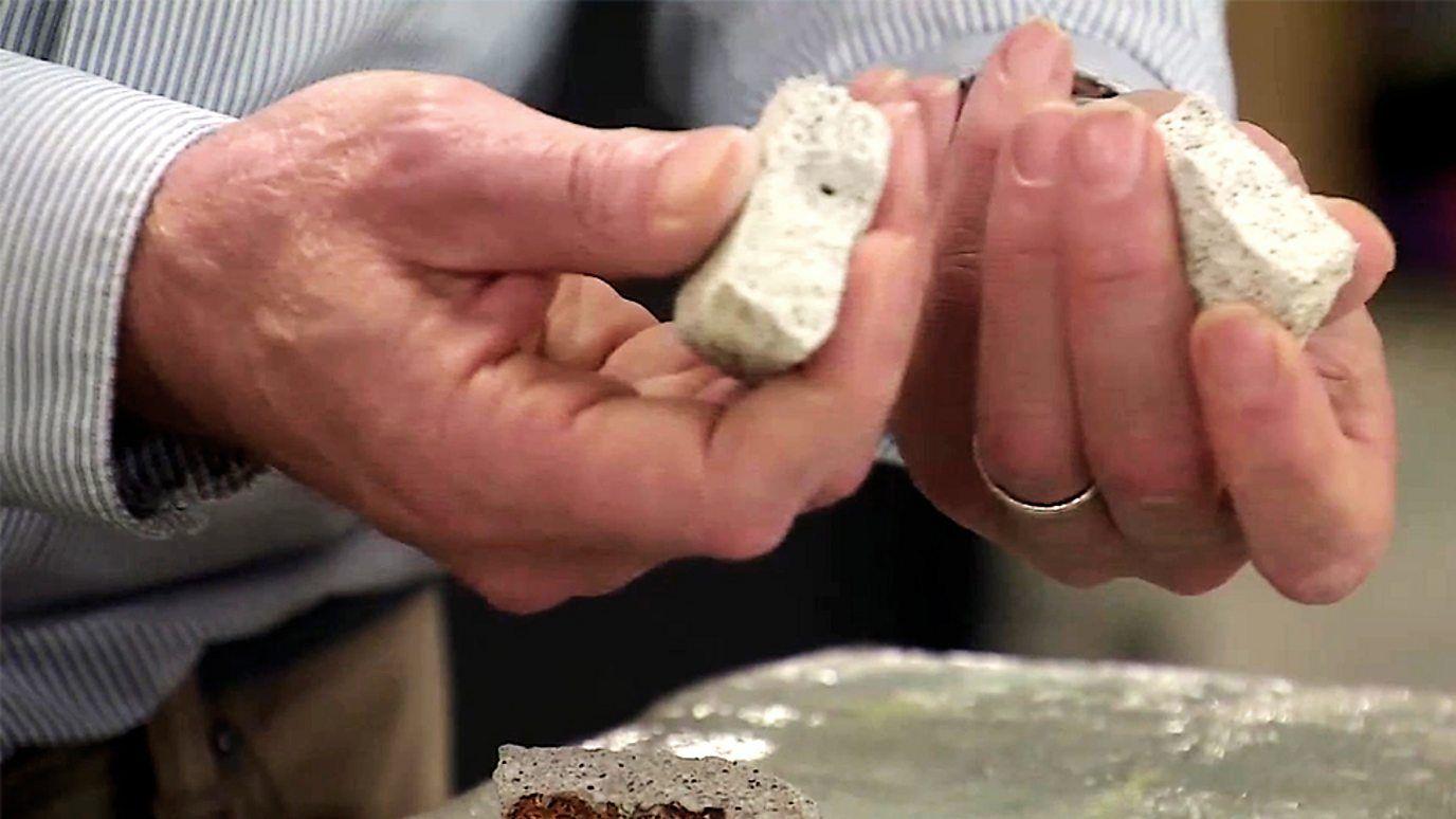 A close-up of two hands holding half a chunk of concrete in each hand.