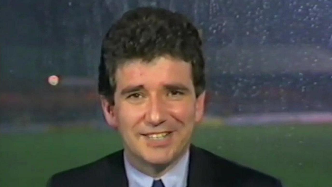 Elton Welsby in a suit presenting live from a studio gallery above a pitch on a rainy night in the 1980s or 90s 