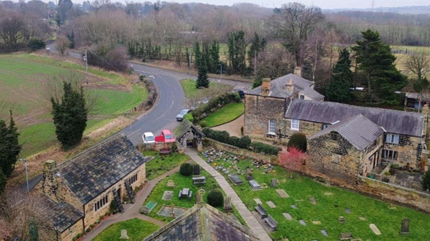 View from St Peter's church tower in Felkirk with a graveyard, open fields and winding road below, and a view of trees, cars, houses and other buildings clustered around the church