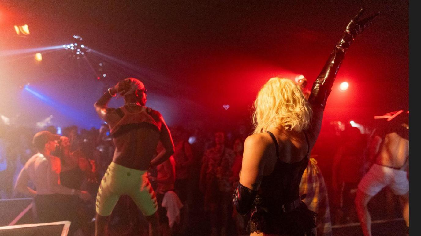 Two dancers at a disco with hands in air and backs to camera in front of a crowd of people