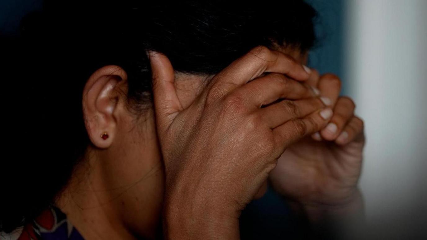 An actor voices the words of a migrant worker in a BBC interview. She has her head in her hands in anguish, shielding her face from view.