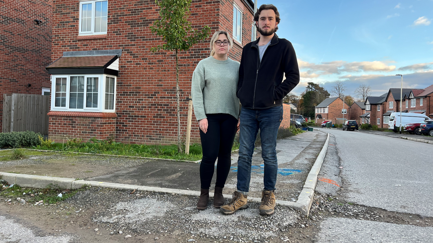 Melissa Brimer and James Evans standing on the pavement on the housing estate. The roads and pavement are in poor quality condition