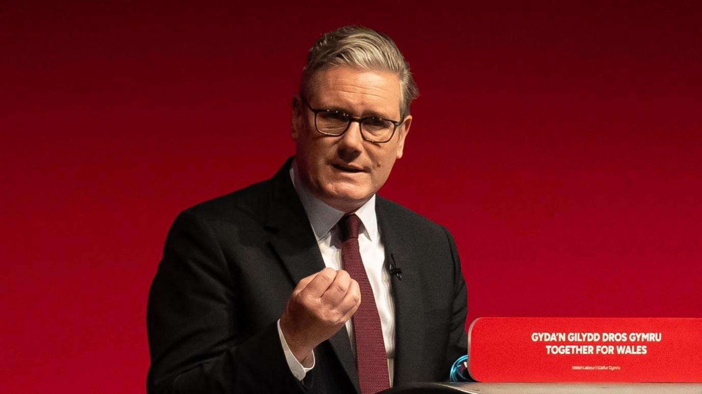 UK Prime Minister Sir Keir Starmer speaks at a lectern in front of a red background.