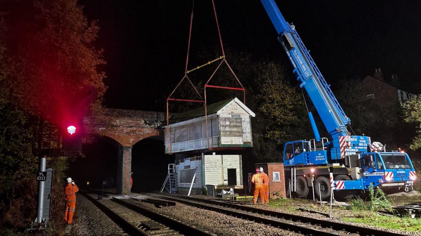 A blue crane is seen removing the top of the signalling box.