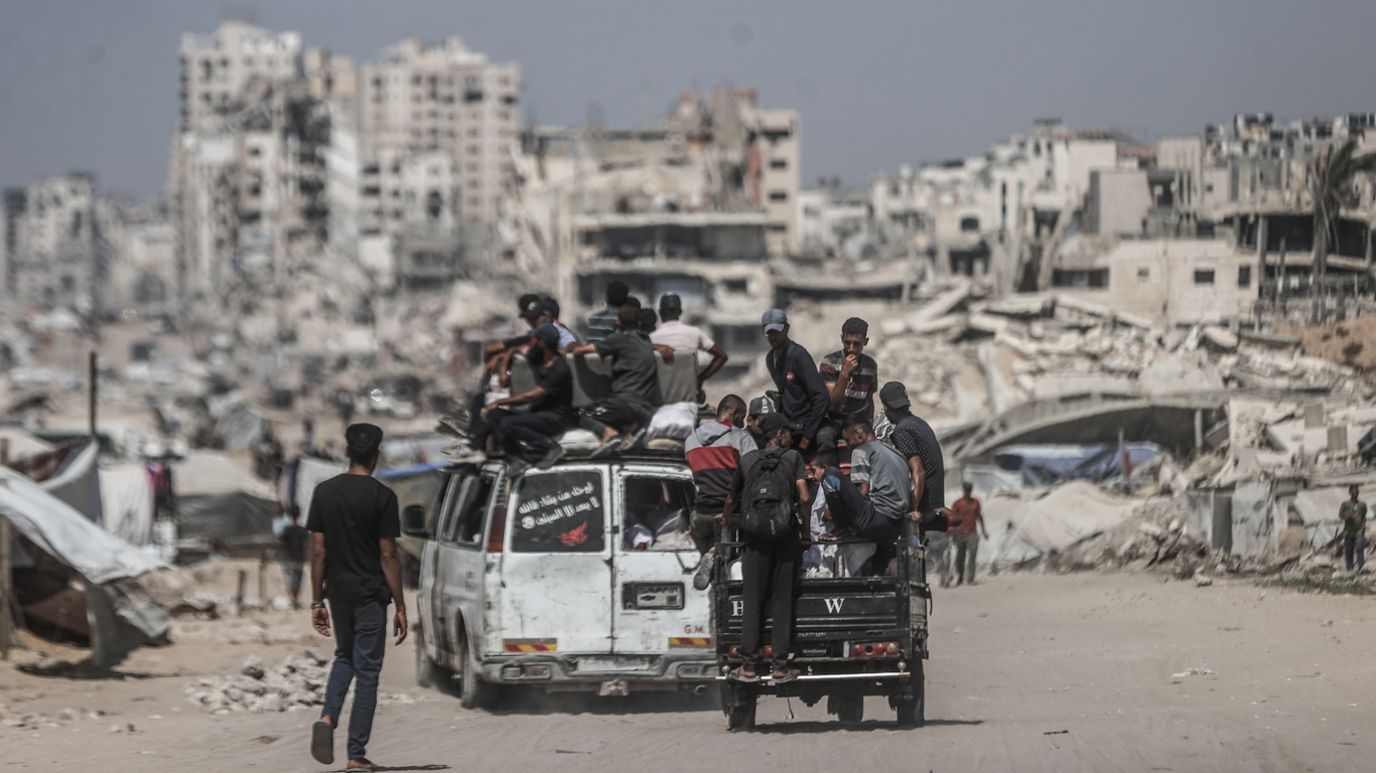 Residents in Gaza City, with buildings destroyed by the Israeli attacks in the background, 24 August