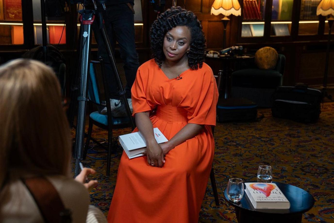 Chimamanda Ngozi Adichie sitting in a chair, listening to Emma Barnett, who is silhouetted in the foregound and is talking