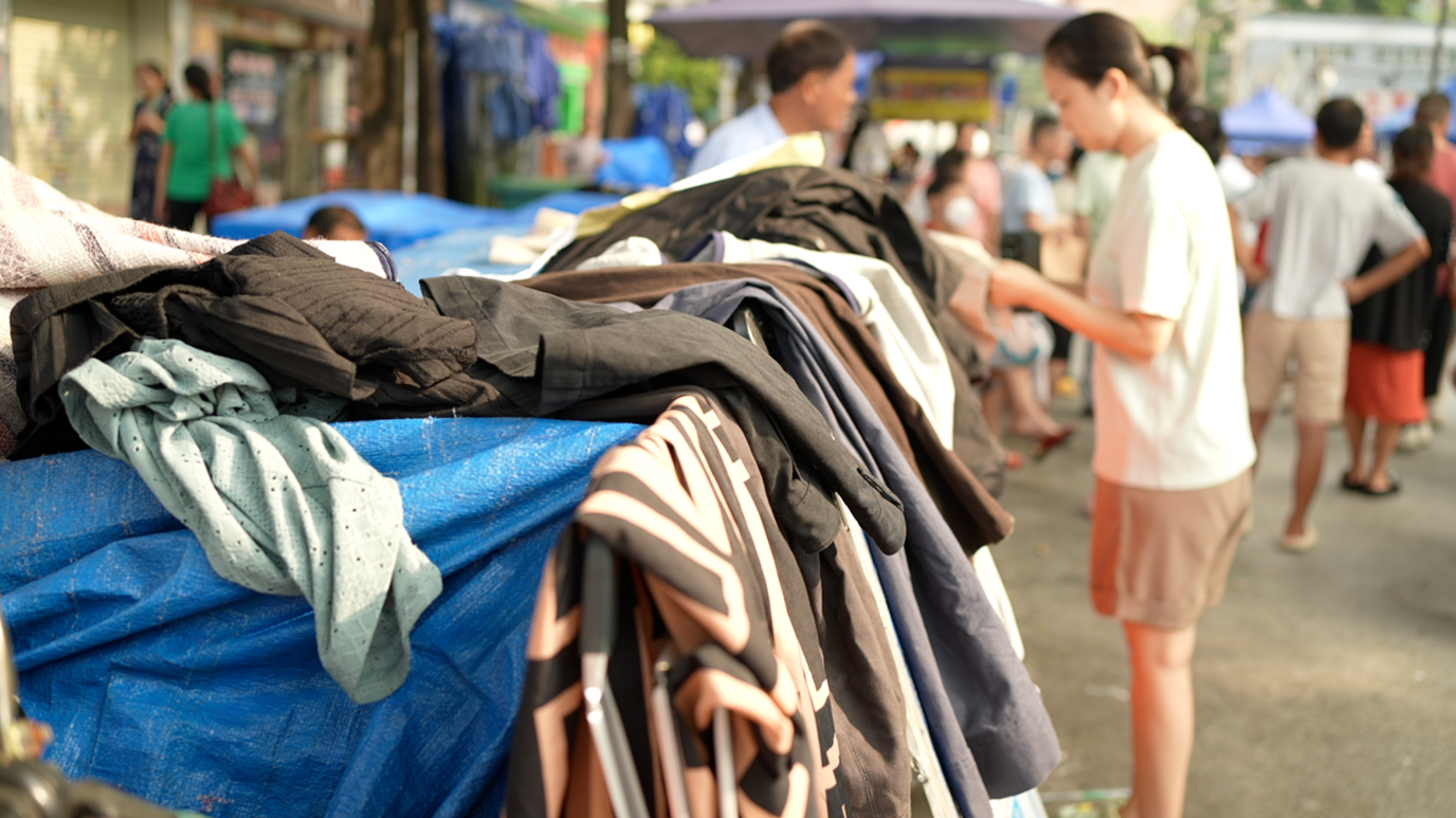 A woman examines the clothes on display on the bulletin boards on a busy street.