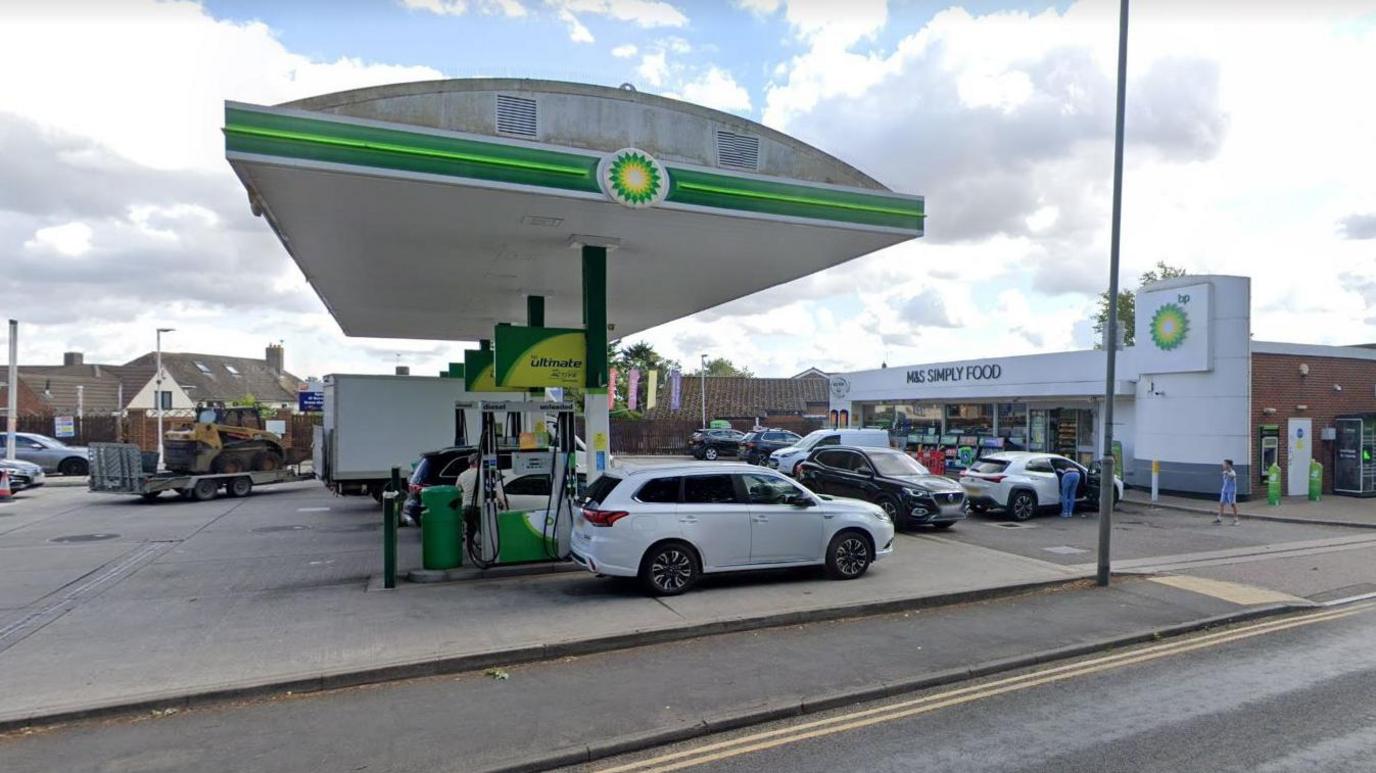 A petrol forecourt with cars parked at the pumps and an M&S Simply Food store in the background.