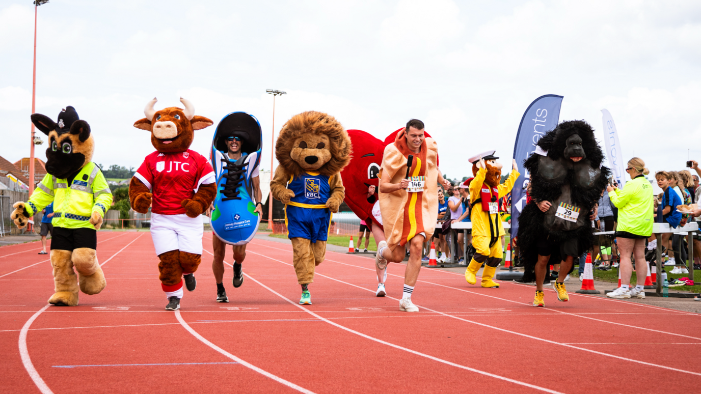 Seven people all dressed in different costumes, competing in a track running race.