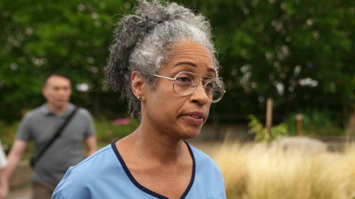 Karen Bonner in her pale blue uniform. She stands outside and wears glasses.