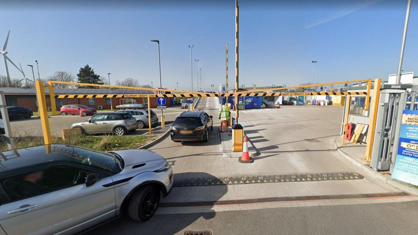 The Avonmouth Bristol waste depot, with cars entering through barrier and man waiting at security. 