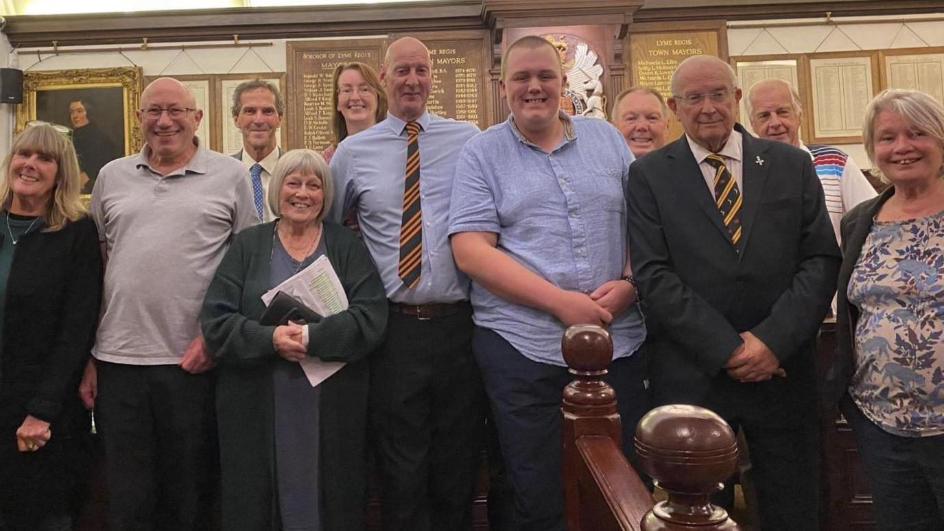 Joshua Denning posing with members of Lyme Regis Town Council in the council chamber