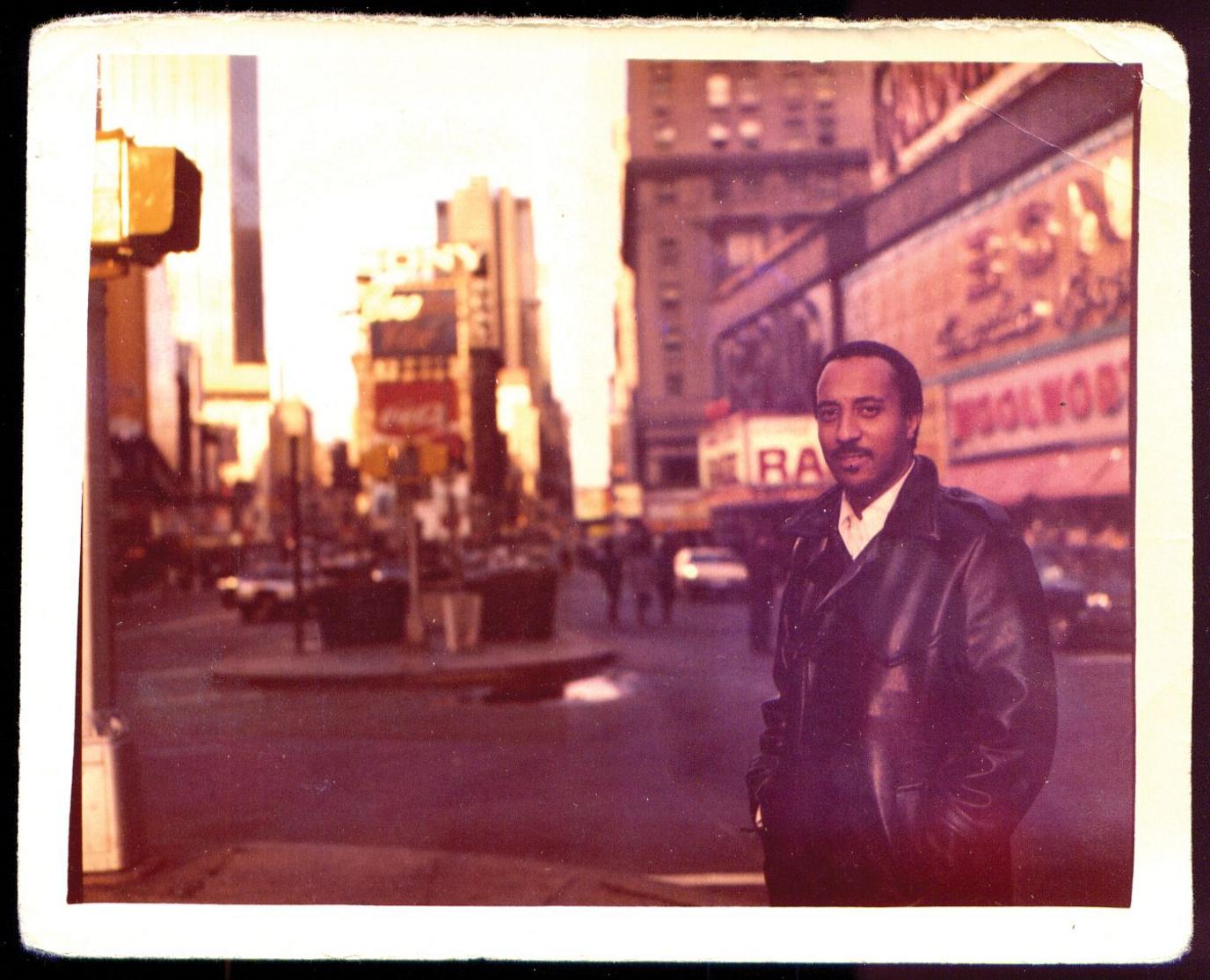 An archive shot surrounded by a white border of Mulatu Astatke wearing a leather jacket and standing in Times Square in New York.