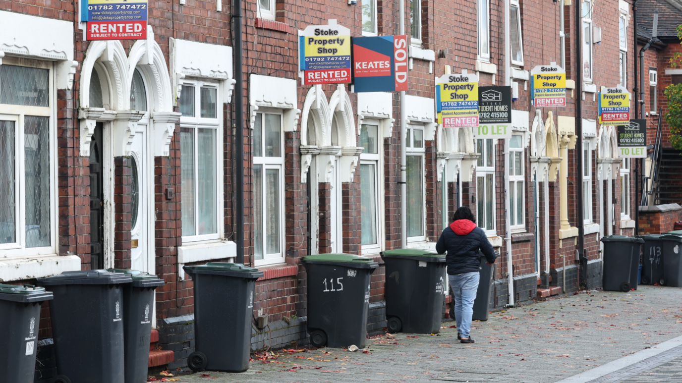 A man walks past a street of terraced houses advertising properties for rent in Stoke-on-Trent