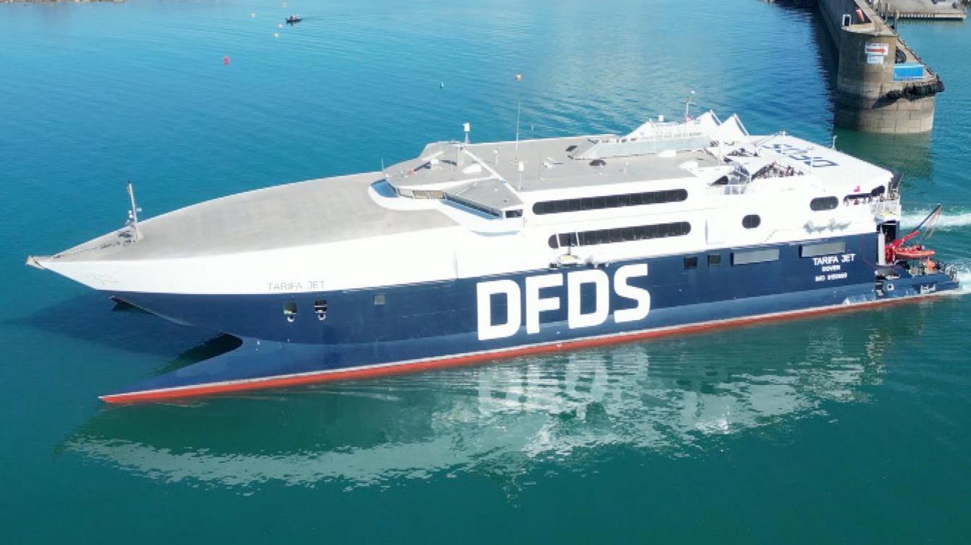 A picture of a large blue body of water with part of the harbour visible. There is a large white and blue boat with DFDS written on its side.