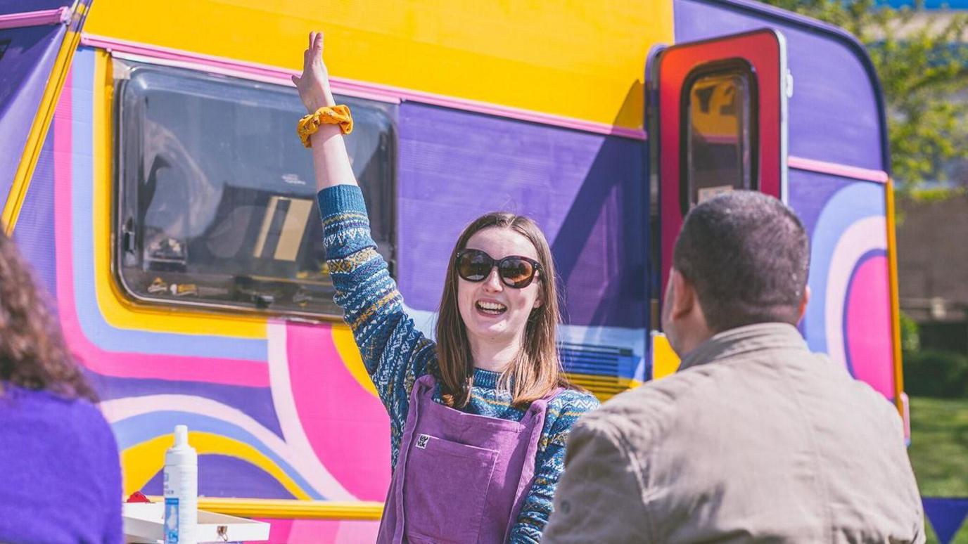 A woman outside a colourful caravan 