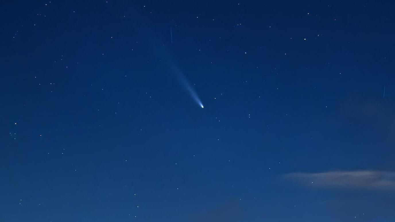 A white comet seen in a dark blue sky with some stars visible