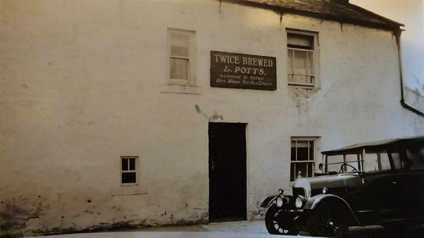 A black and white film photograph from 1930 showing a pub with a sign reading 'Twice Brewed  L. POTTS.'. It is a white building with small windows and a motorcar parked up outside. 