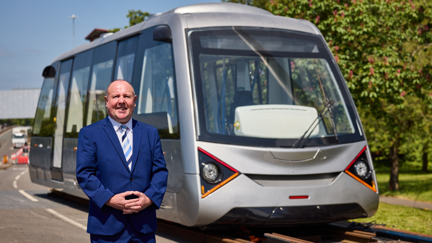 Councillor Jim O'Boyle, who is standing in a road, with a silver VLR vehicle behind him.