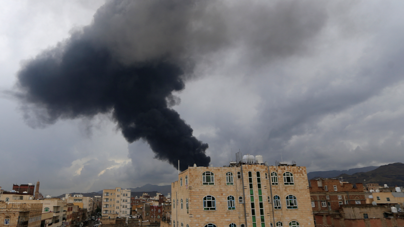 A large plume of black smoke rising behind a red-bricked building in Sanaa, one of may including blocks of flats