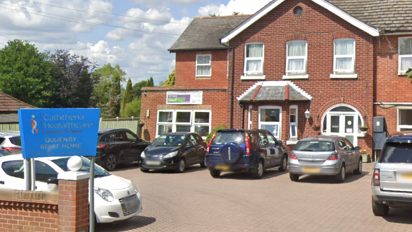 A view of of the front of Quenby Rest Home as seen on Google streetview. Several cars are parked outside the building which displays its previous "good" rating from the CQC on the wall.