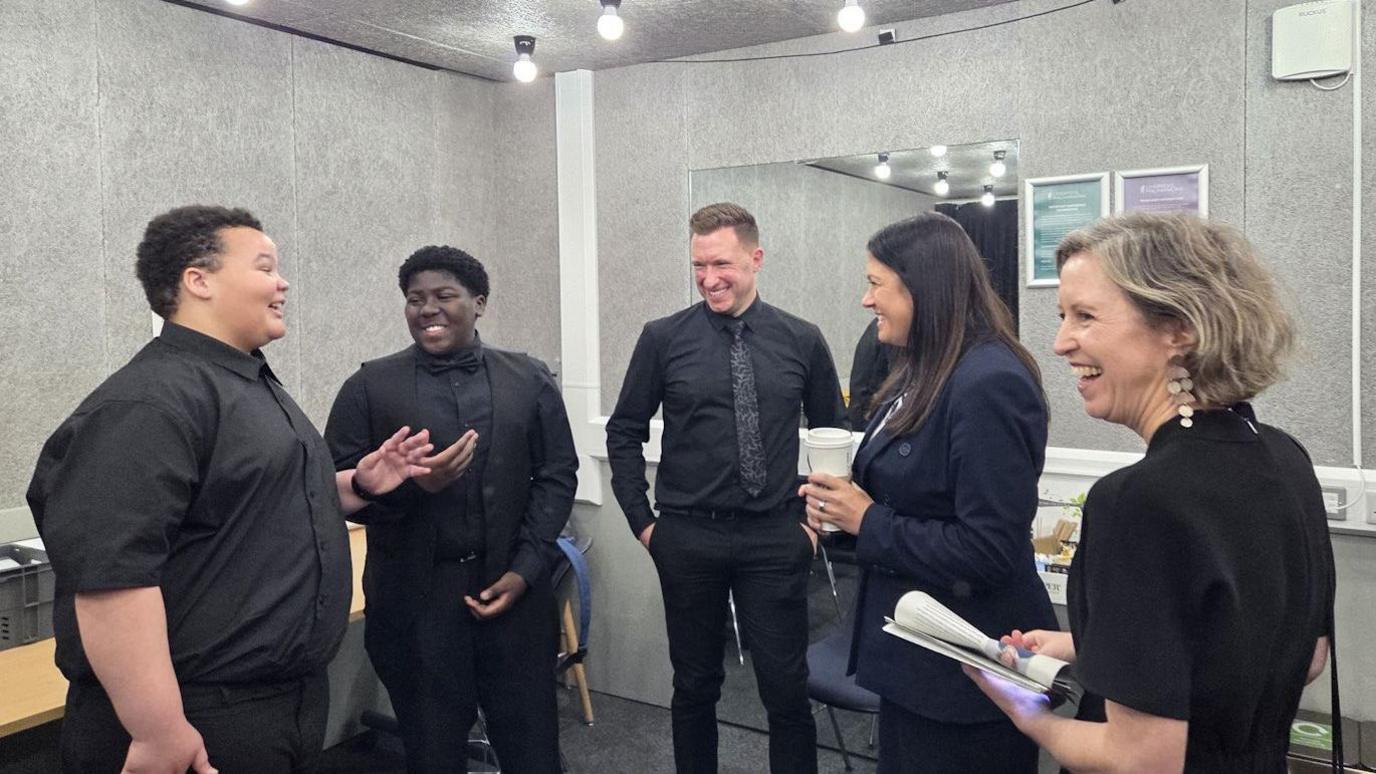 Two boys dressed in black shirts are smiling as they talk with Lisa Nandy and other Liverpool Philharmonic representatives
