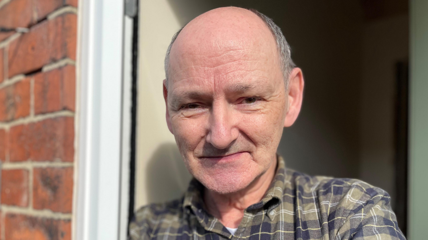 Ross Hopkins, pictured outside his house in Midland Terrace. He is wearing a green and blue chequered shirt, and has grey hair that has receded 