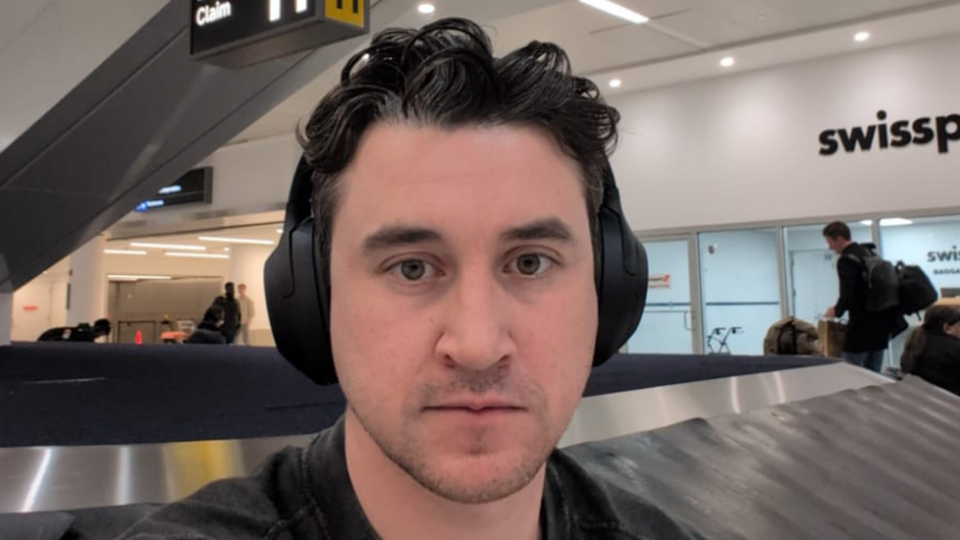 William takes a selfie whilst wearing headphones infront of a luggage carousel at JFK airport