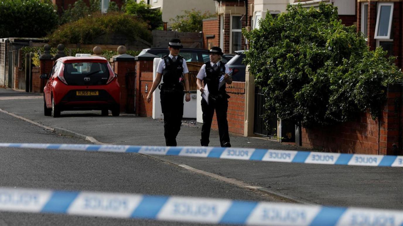 Police officers walk near the scene in Hart street where the boy was arrested after people were stabbed in Southport.