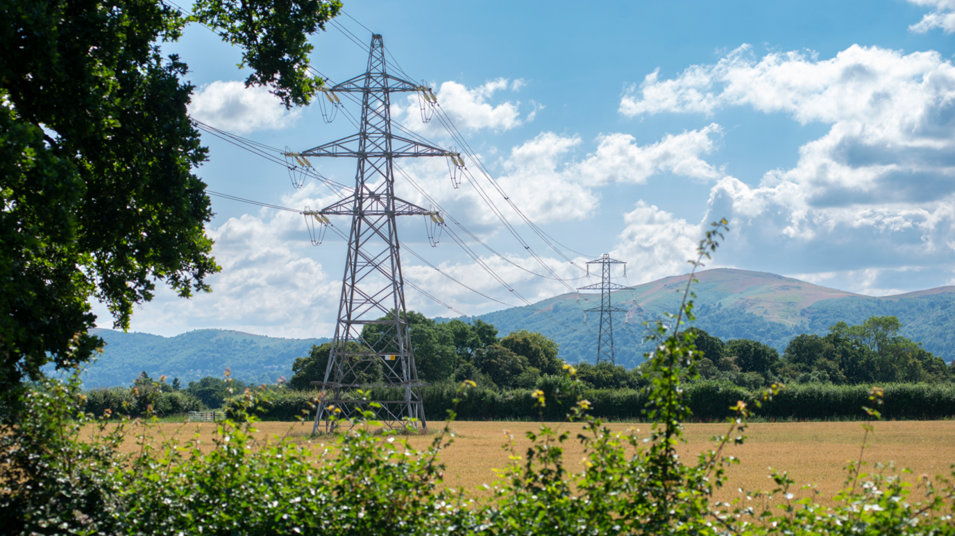 Pylons in fields with power lies and hills in the background