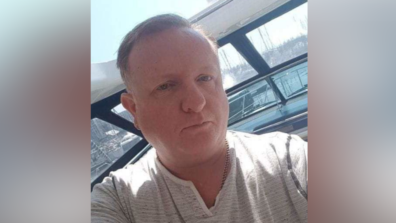 Mark Worship is pictured in a selfie-style photo while on board his boat. He has no expression on his face and the front of his boat can be seen behind him. He has short grey hair and he is wearing a white and grey coloured top with a chain around his neck.