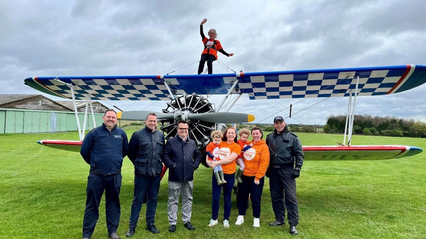 Josie Howley on the wings of a Boeing Stearman bi-plane with a group of people beneath her