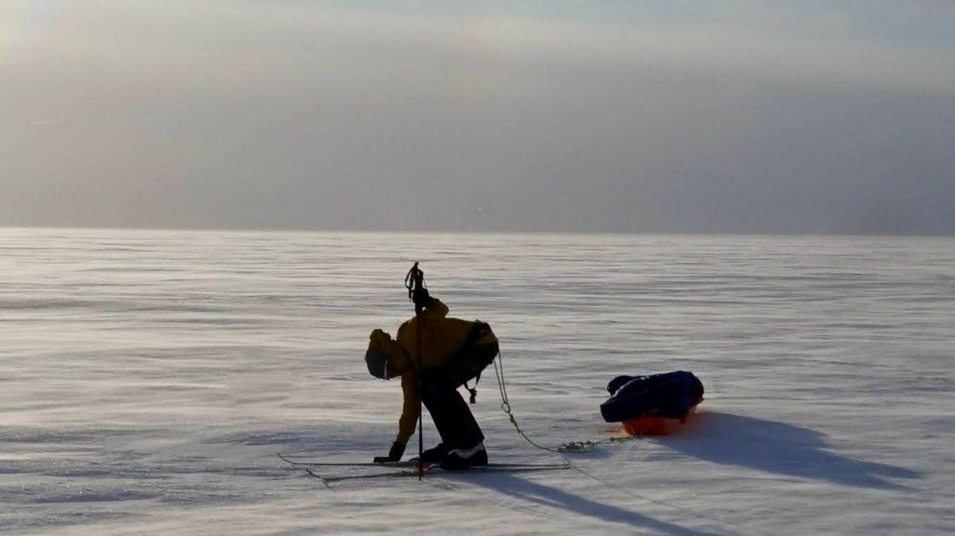 Frederick Fennessy on skis pulling a sled across snow - there is only snow and blue sky visible in the background.