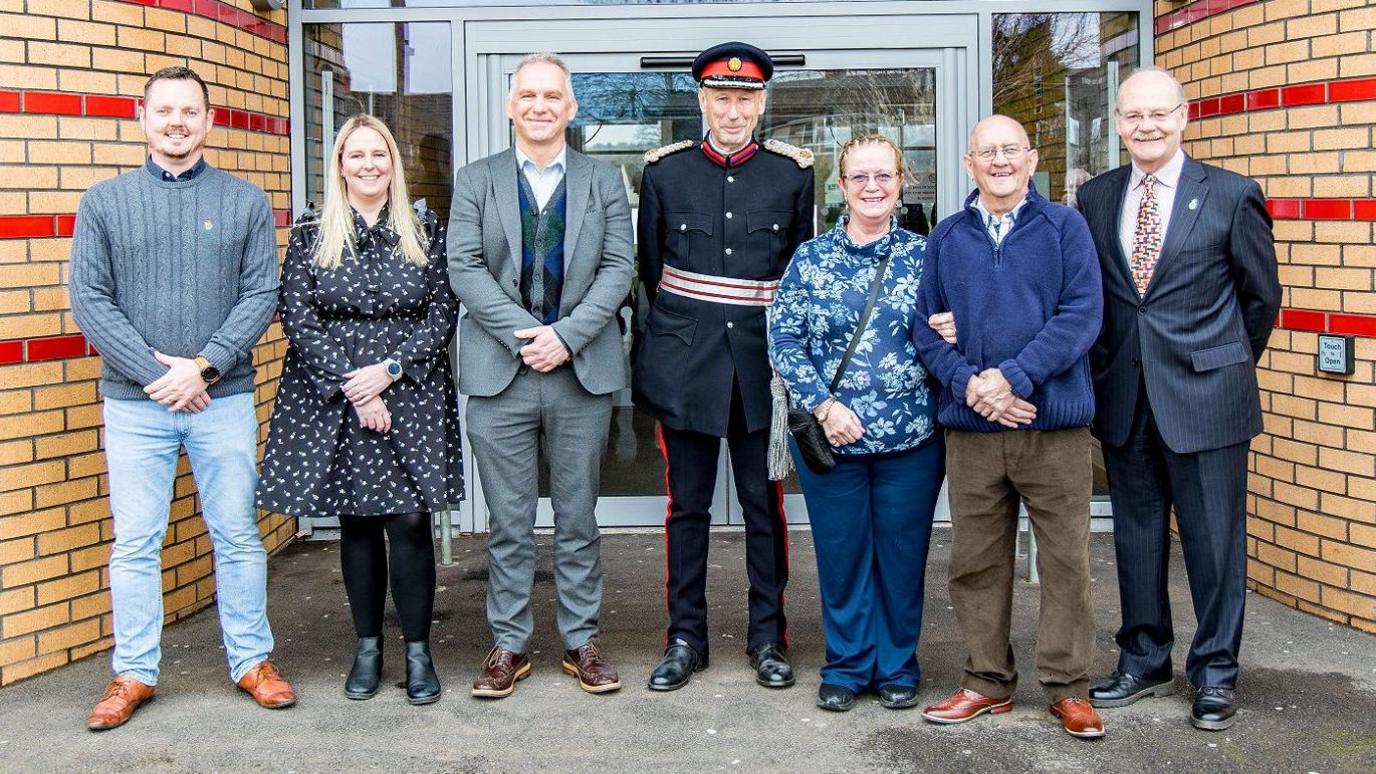 A group of smartly-dressed people stand outside the Coronation Centre in Cadbury Heath, a building with neat light-coloured brickwork on its exterior