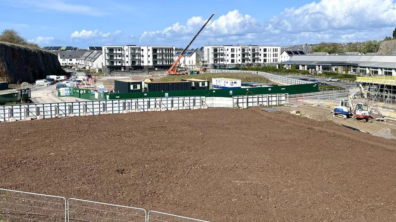 A photo showing the proposed land for the care home. The land has been dug up and there are several cranes around the area as well as fencing keeping people out and new flats.