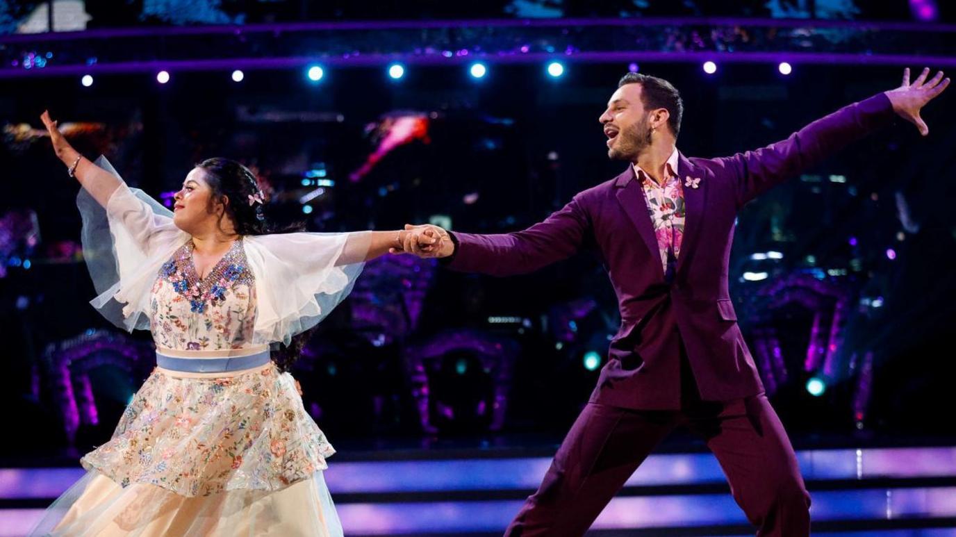 Ellie Goldstein and Vito Coppola dancing on the TV show Strictly Come Dancing. She is wearing a colourful dress and Coppola is wearing a purple suit.