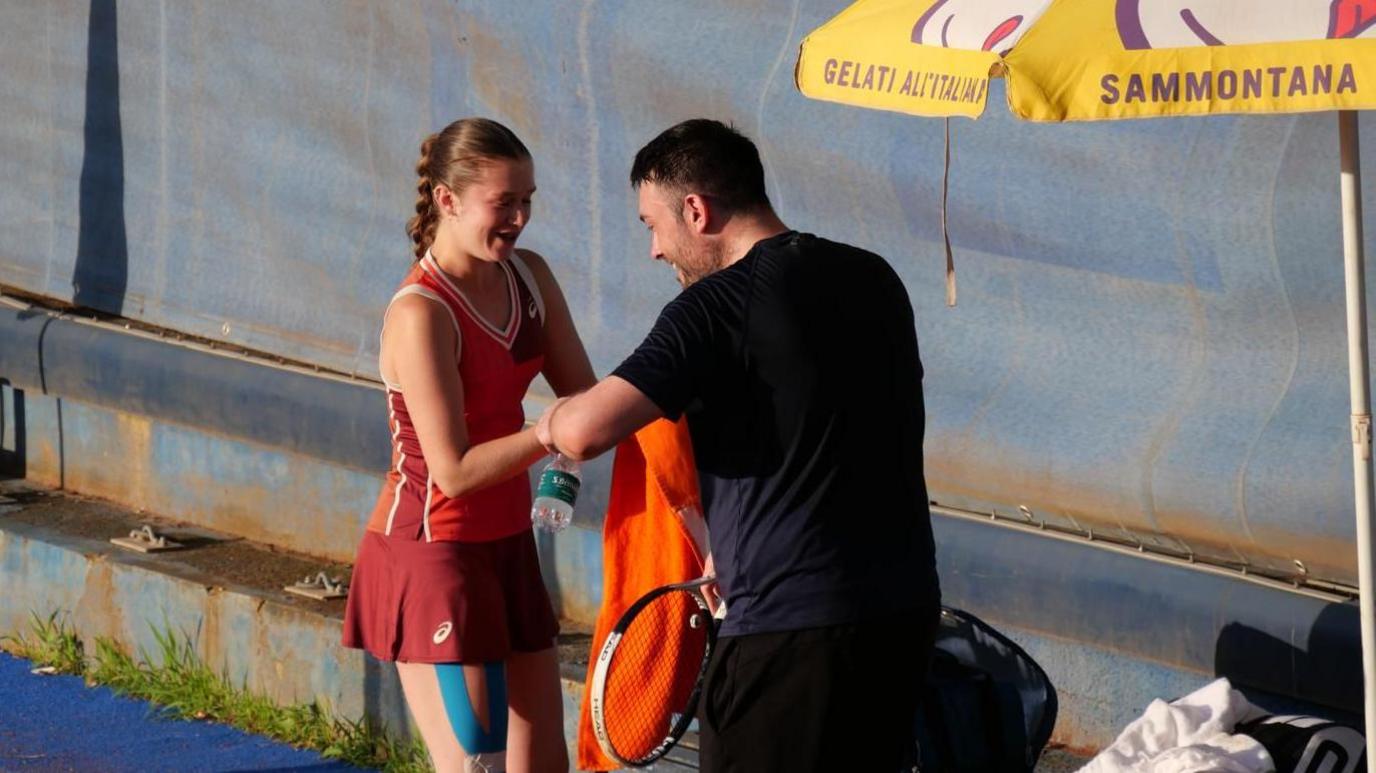 Georgia Routledge speaks to a member of her team on the side of the court during a break in play, in the middle of a match.