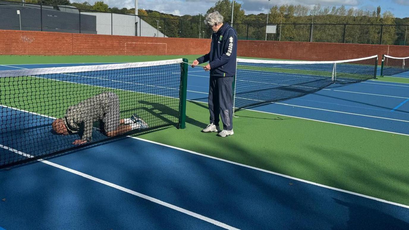 A man kneels down kissing a green and blue tennis court