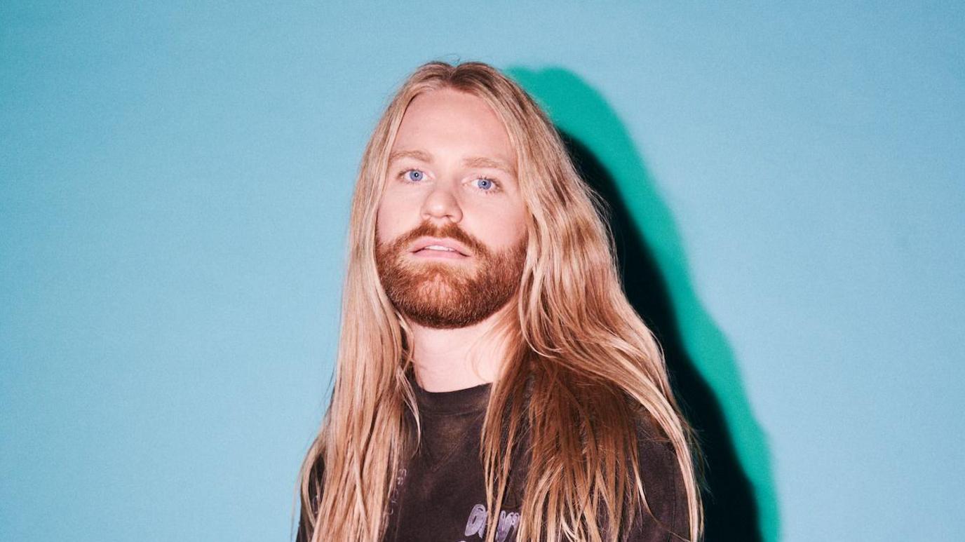 A man with long blonde hair and a blonde/ginger beard staring into the camera