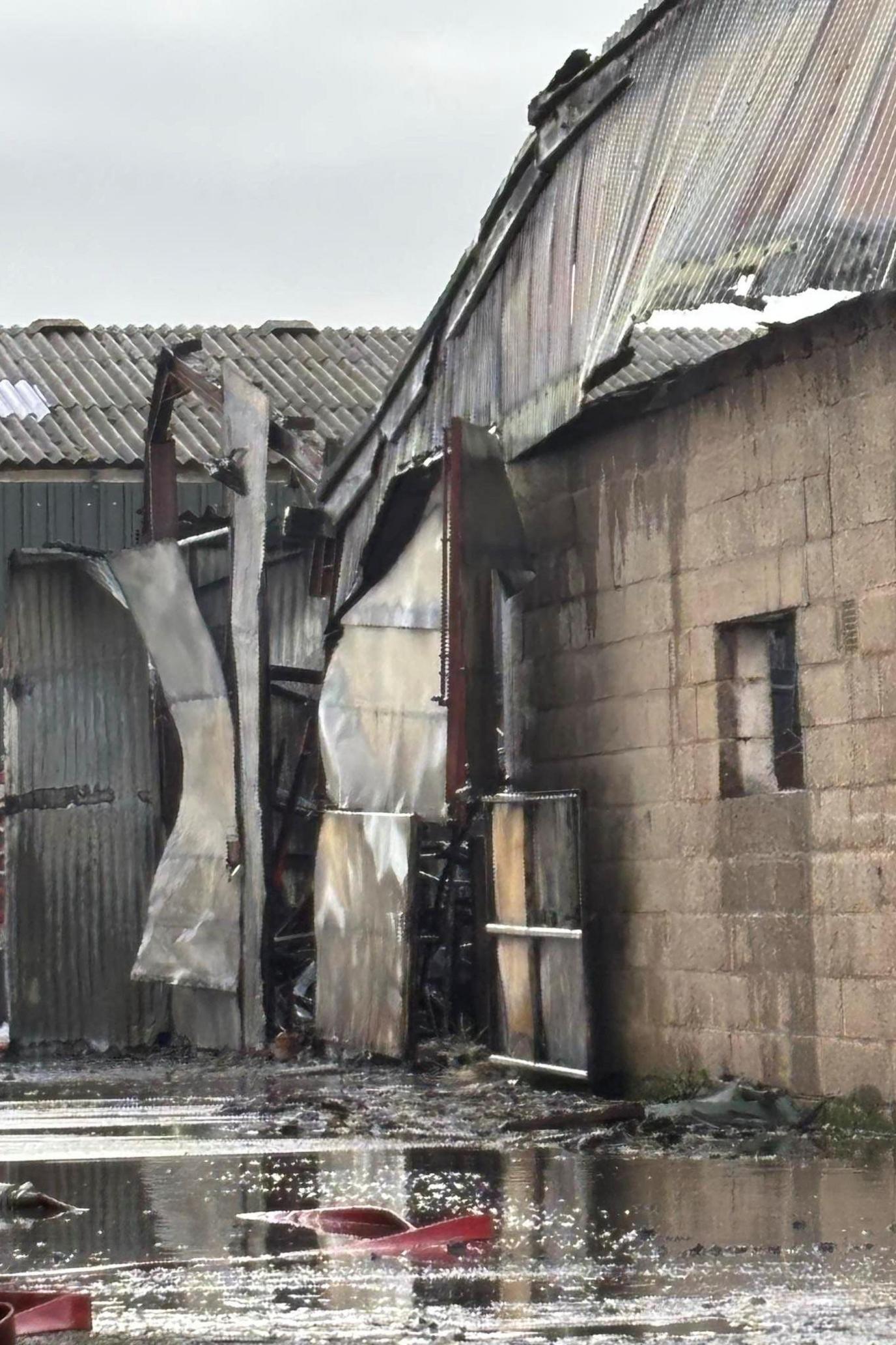 A close-up of a fire-damaged building with a buckled roof, parts coming away and water around the walls after the firefighters put out the blaze.