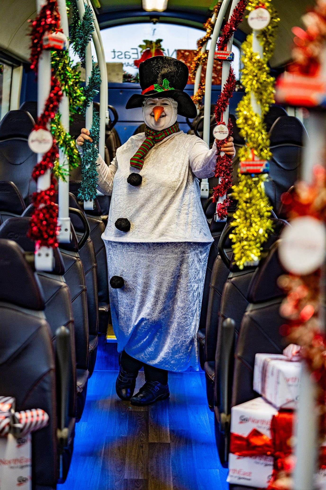 Julie Richardson standing on a bus dressed as a snowman. She has a carrot as a nose.