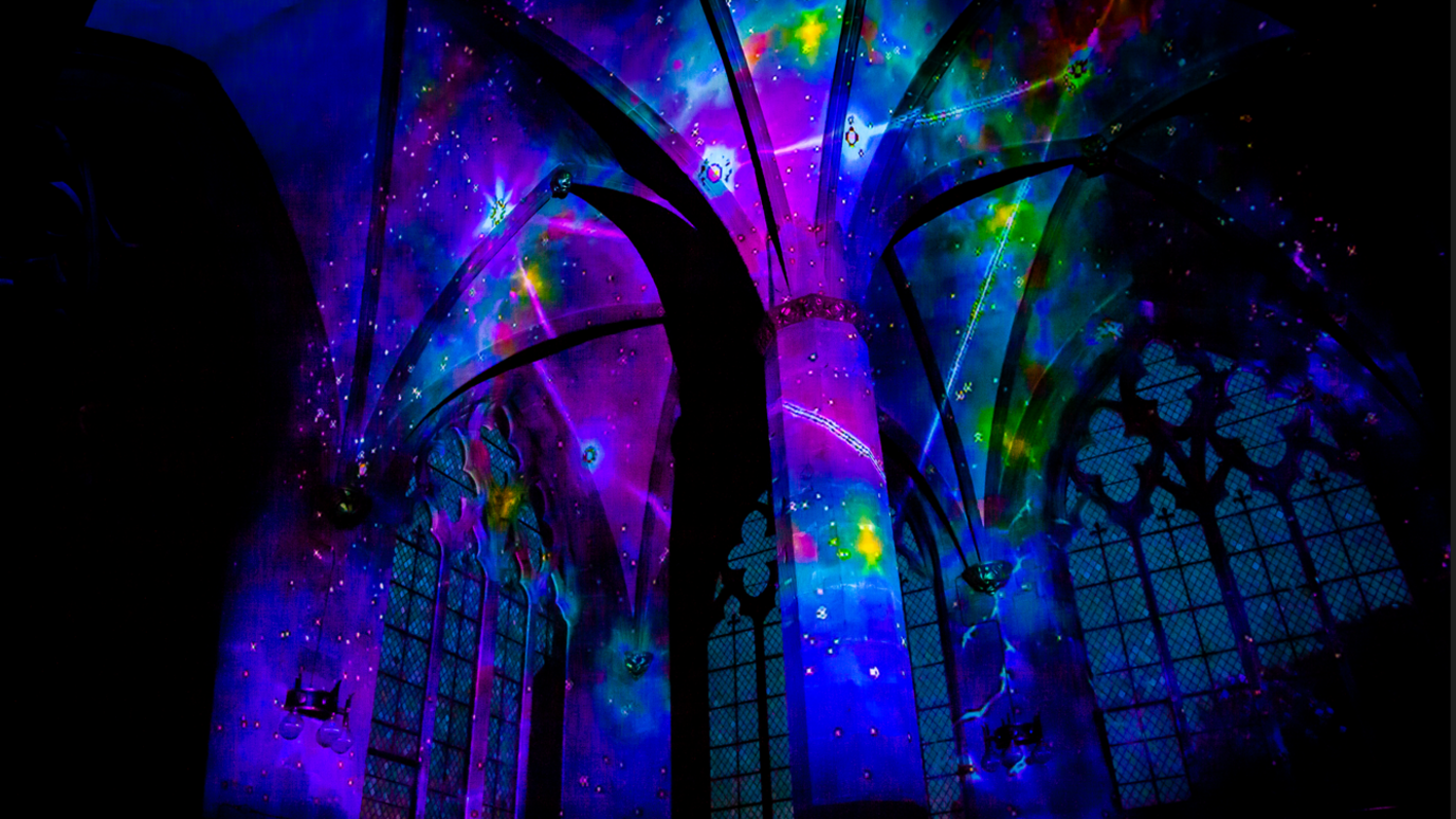 A cathedral ceiling and arched window lit up in blue, pink, purple and green lights