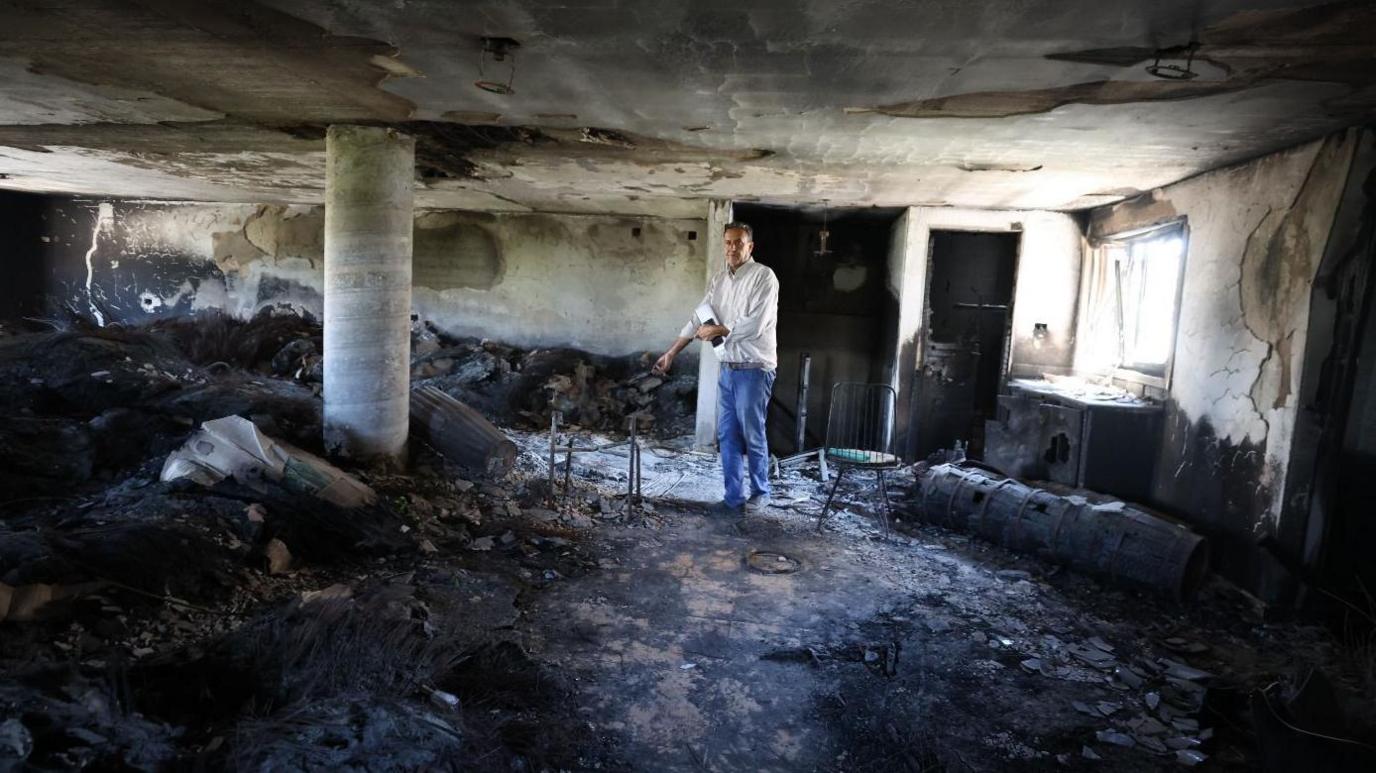 A man stands inside a burnt room.