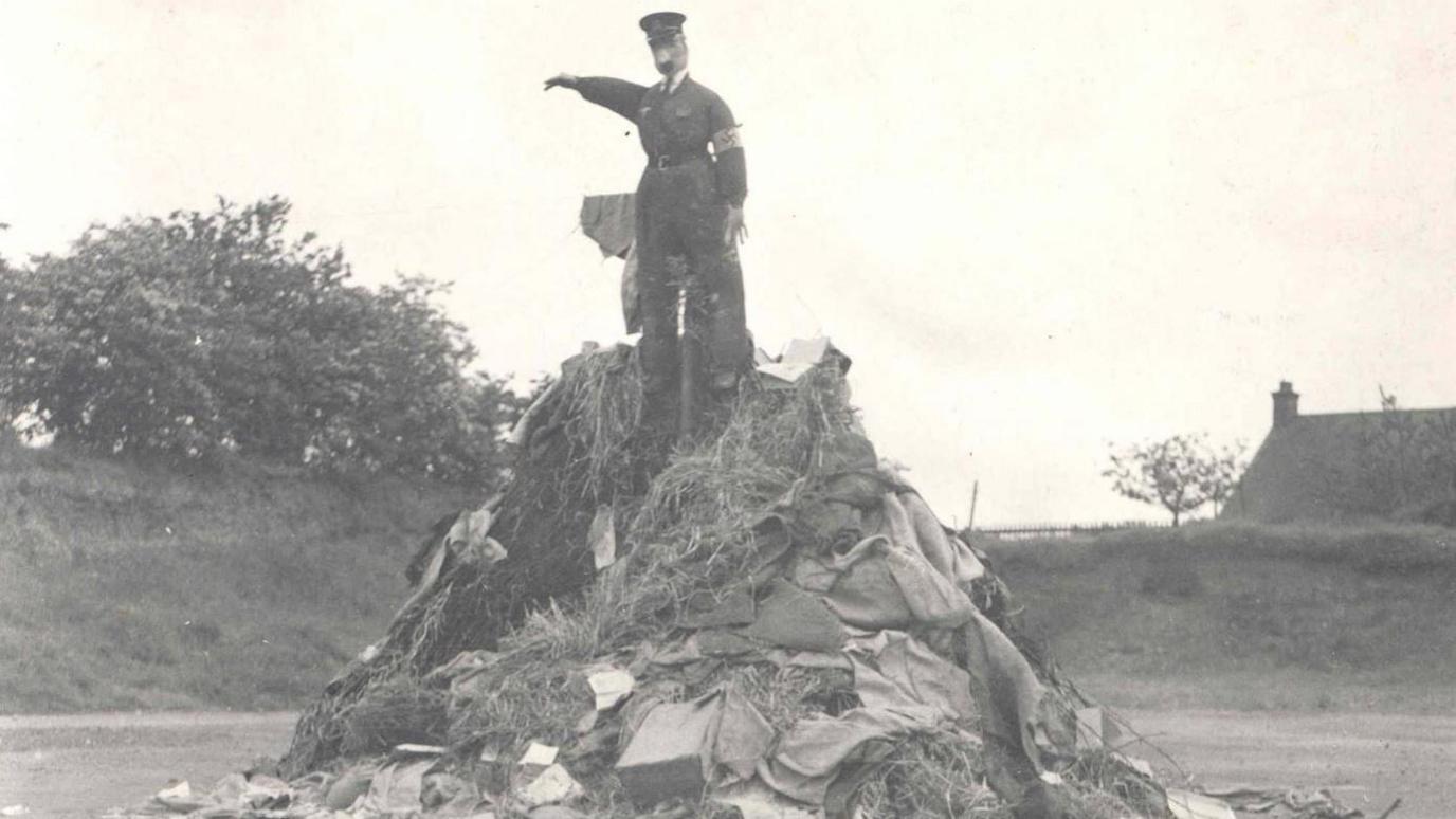 A black and white photo shows an unlit bonfire with and effigy of Hitler at the top.