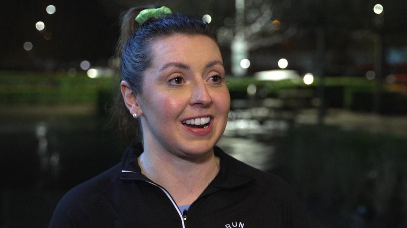 A woman with dark hair in a pony tail and a dark running top